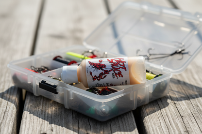 Fishing tackle box with lures and a bottle on a wooden surface